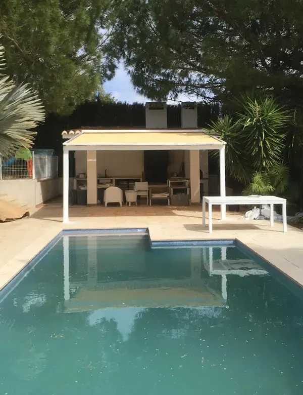 Pérgola de aluminio con toldo plano instalado en zona de piscina de jardín residencial.